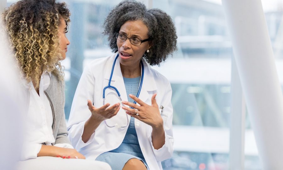 Serious mature female doctor gestures while talking with a young adult female patient.